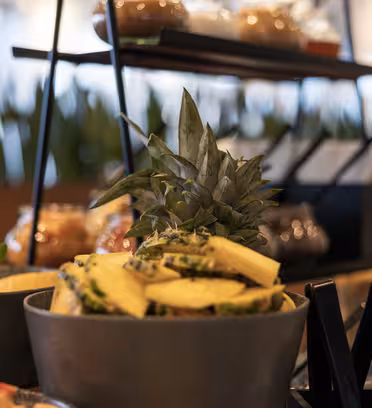 En visning av ferske ananasskiver og mynte i skåler arrangert på et buffébord. I bakgrunnen, ute av fokus, er ytterligere beholdere med mat og bladplanter.