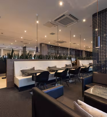 Moderne restaurantinteriør med svart og hvit dekor. Har svarte stoler, hvite bord og kremboder. Planter separate seksjoner, med hengende lys og mønstrede vegger som forbedrer stemningen. Taket har innfelt belysning og klimaanlegg.
