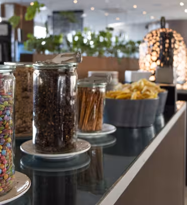 Et moderne bufféoppsett med krukker fylt med fargerike godterier, nøtter, kringler og en bolle med chips. Bakgrunnen har planter og stilig belysning som gir rommet et moderne preg.